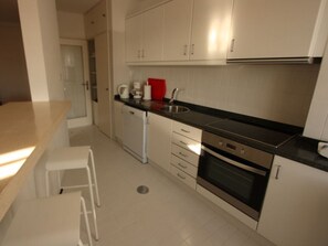 Uma cozinha compacta com armários brancos, bancada preta, cafeteira e pia.