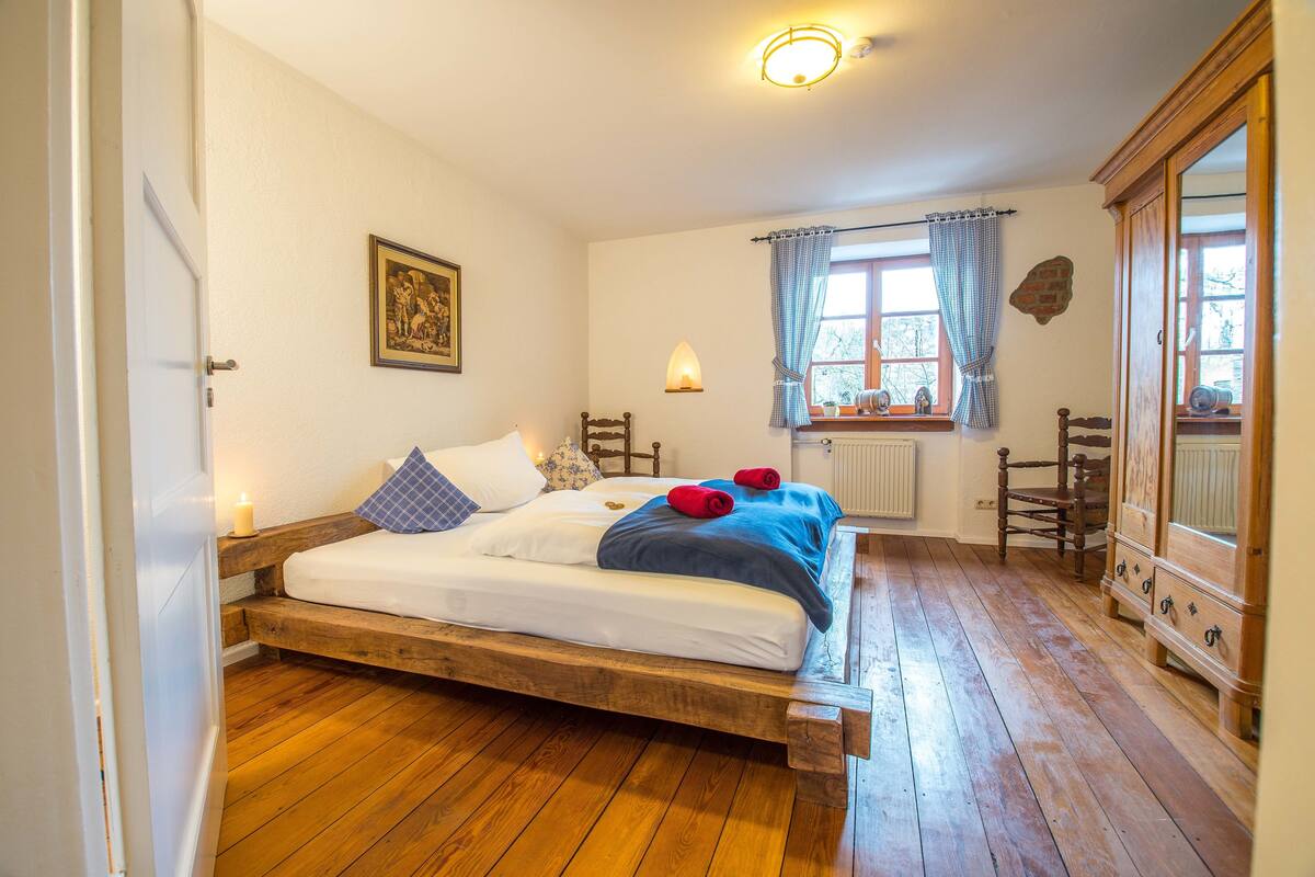 Ein Holzbett in einem Zimmer mit Fenster, Heizkörper und Holzschrank.