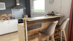 A modern kitchen with a wooden island, two bar stools, a window with a view, and a clock on the wall. - Large and spacious for max. 6 guests with great views (St. Andreasberg)