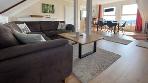 A modern living room with a brown leather sofa, a wooden coffee table, and a dining area with a table and chairs. - Large and spacious for max. 6 guests with great views (St. Andreasberg)