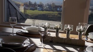 A dining table set with plates, glasses, and candles, with a view of houses and hills through a window. - Large and spacious for max. 6 guests with great views (St. Andreasberg)