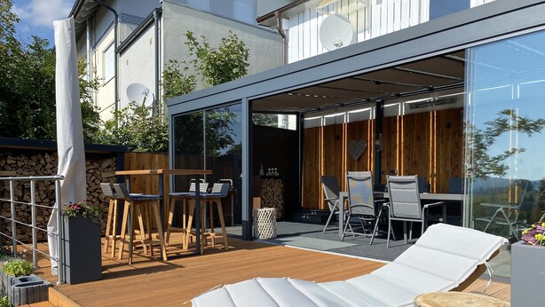 A modern outdoor patio with wooden furniture, a lounge chair, and a glass-enclosed dining area. - Large and spacious for max. 6 guests with great views (St. Andreasberg)