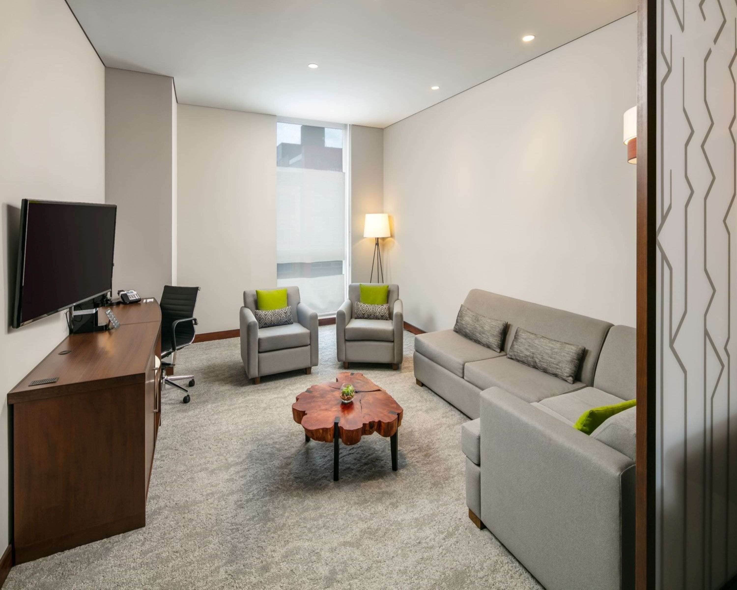 A modern living room with a flat-screen TV, two armchairs, a sofa, a coffee table, and a lamp.