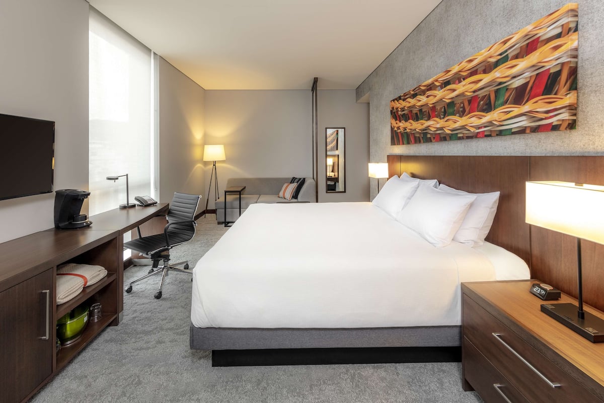 Habitació d'hotel amb un llit gran, una taula de treball amb un ordinador, una cadira, un televisor i un quadre a la paret.