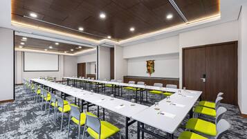 A conference room with long tables, chairs, and a projector screen.