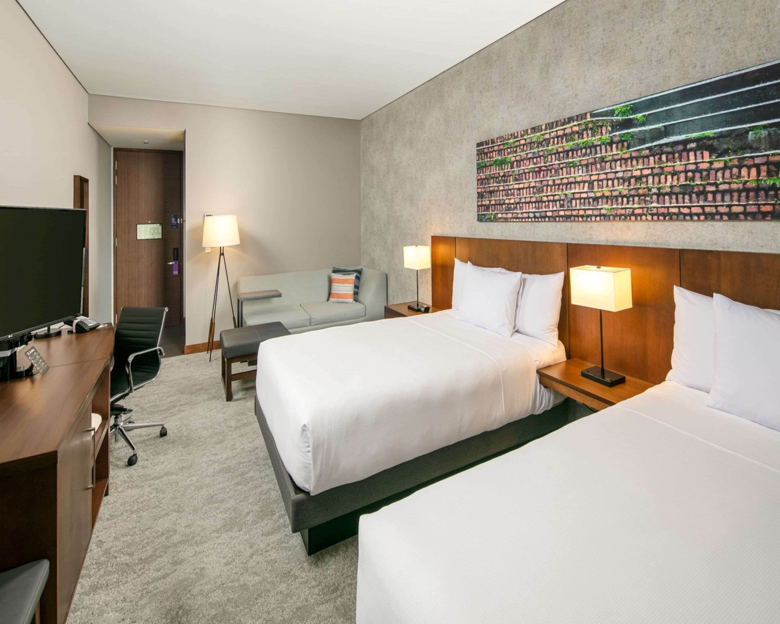 A hotel room with two beds, a desk with a computer, a TV, and a large wall mural.