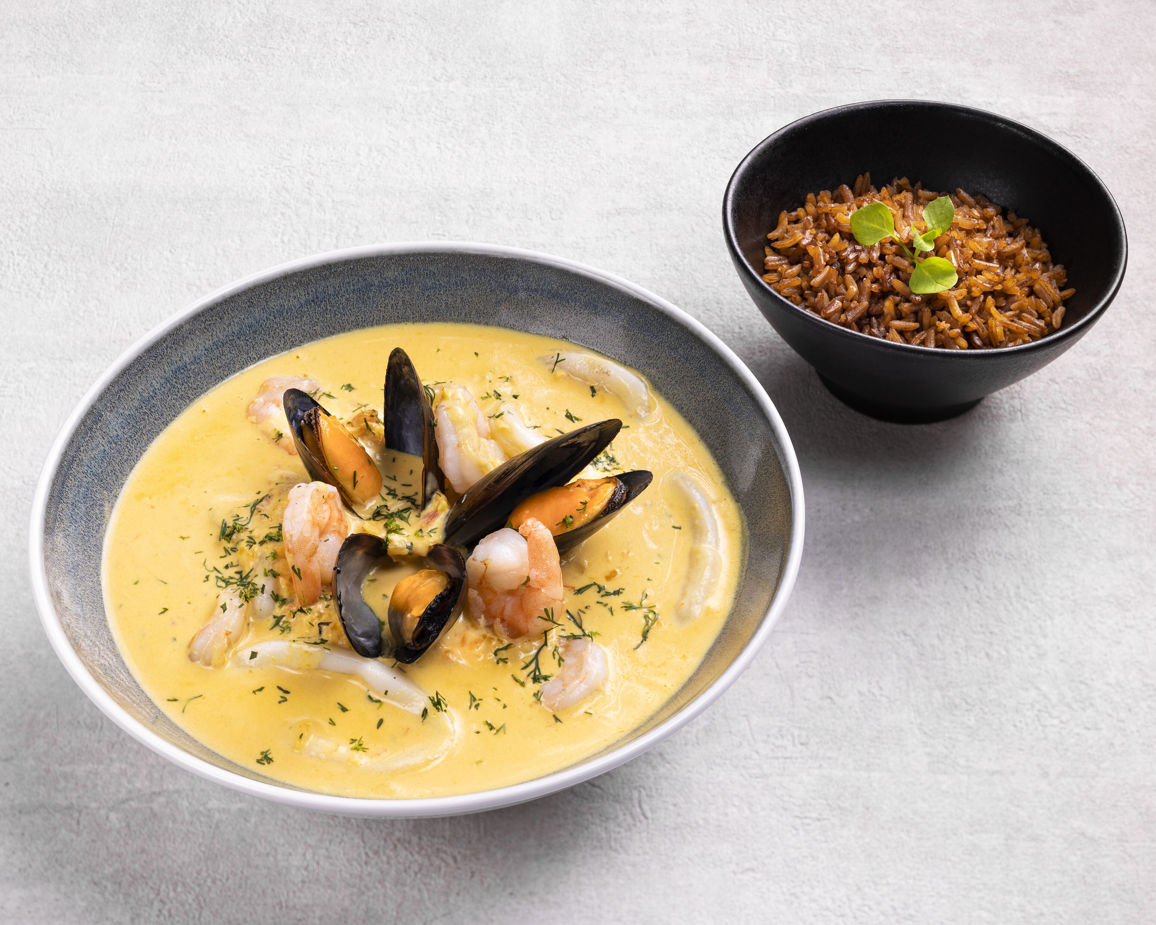 Un plato de sopa de mariscos con mejillones y camarones, acompañado de arroz integral.
