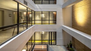 Un atrium à plusieurs niveaux avec des rampes en verre, un espace central ouvert doté d’un sol à motifs et un mur de briques sur l’un des côtés.