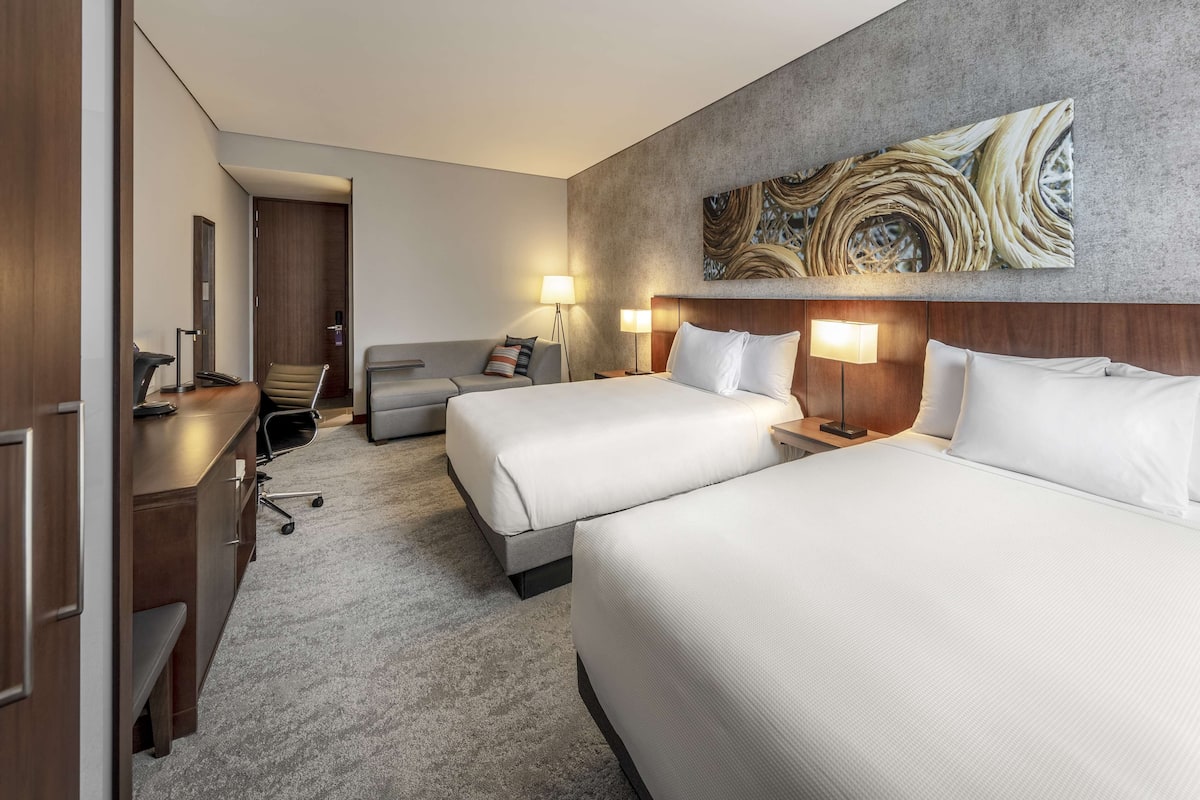 Una habitació d'hotel amb dos llits, una taula, una cadira i un quadre abstracte gran a la paret.
