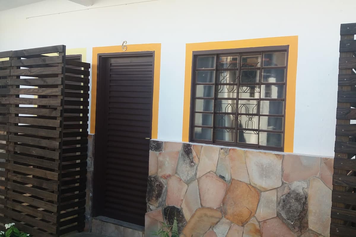 Une maison avec un mur en pierre, un portail en bois et une fenêtre ornée d’une grille métallique.