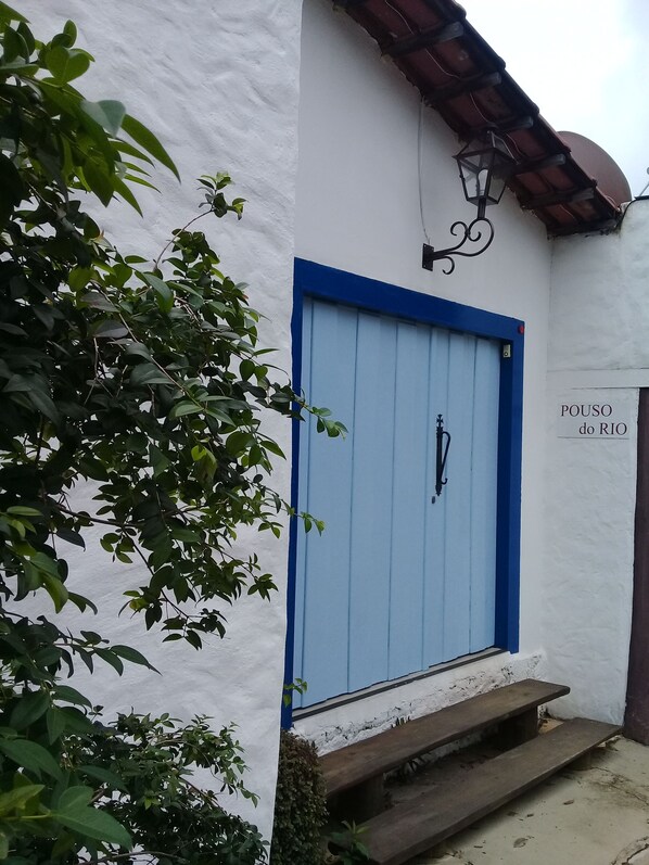 A building with a blue door, a sign reading "POUSO do RIO", and a small wooden bench outside.