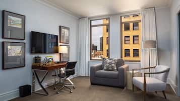 Habitación de hotel con escritorio, dos sillas, sofá y un ventanal con vista a la ciudad.