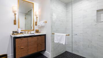 A modern bathroom with a marble shower, a wooden vanity, and a large mirror with wall sconces.