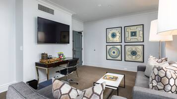Una sala de estar moderna con un televisor de pantalla plana, un escritorio con una silla, un sofá y una mesa de centro. Hay cuatro obras de arte enmarcadas en la pared.