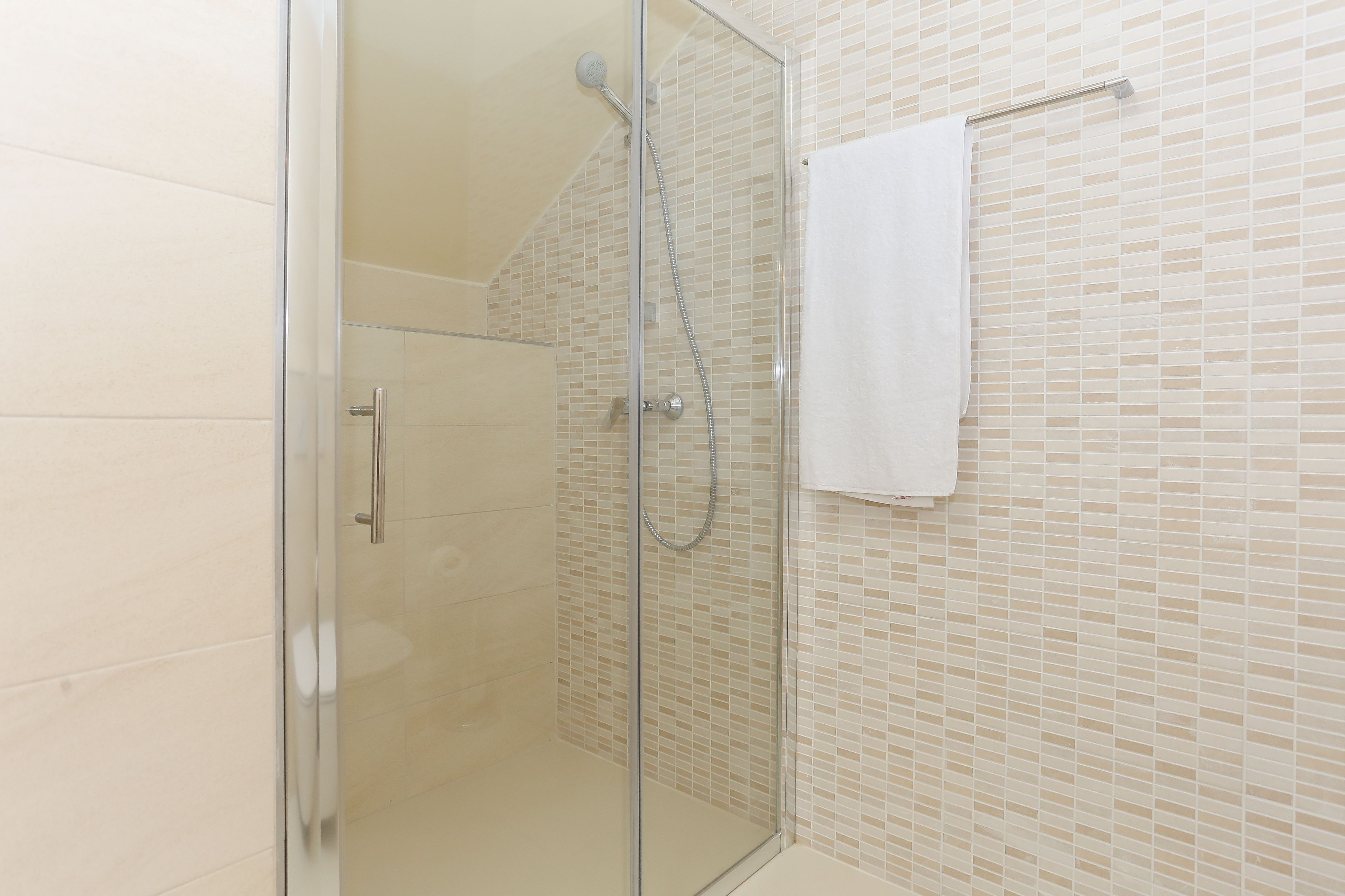 A glass-enclosed shower with a handheld showerhead and a towel rack with a white towel.