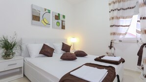 A hotel room with a double bed, a bedside table, a lamp, a potted plant, and abstract wall art. - The Tribunj Suites (Tribunj)