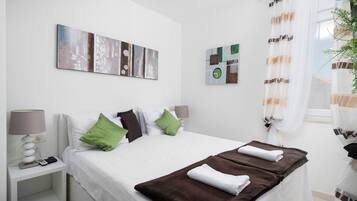 Une chambre d’hôtel avec un lit, des oreillers, une table de chevet, une lampe, des œuvres d’art au mur et une fenêtre avec des rideaux.