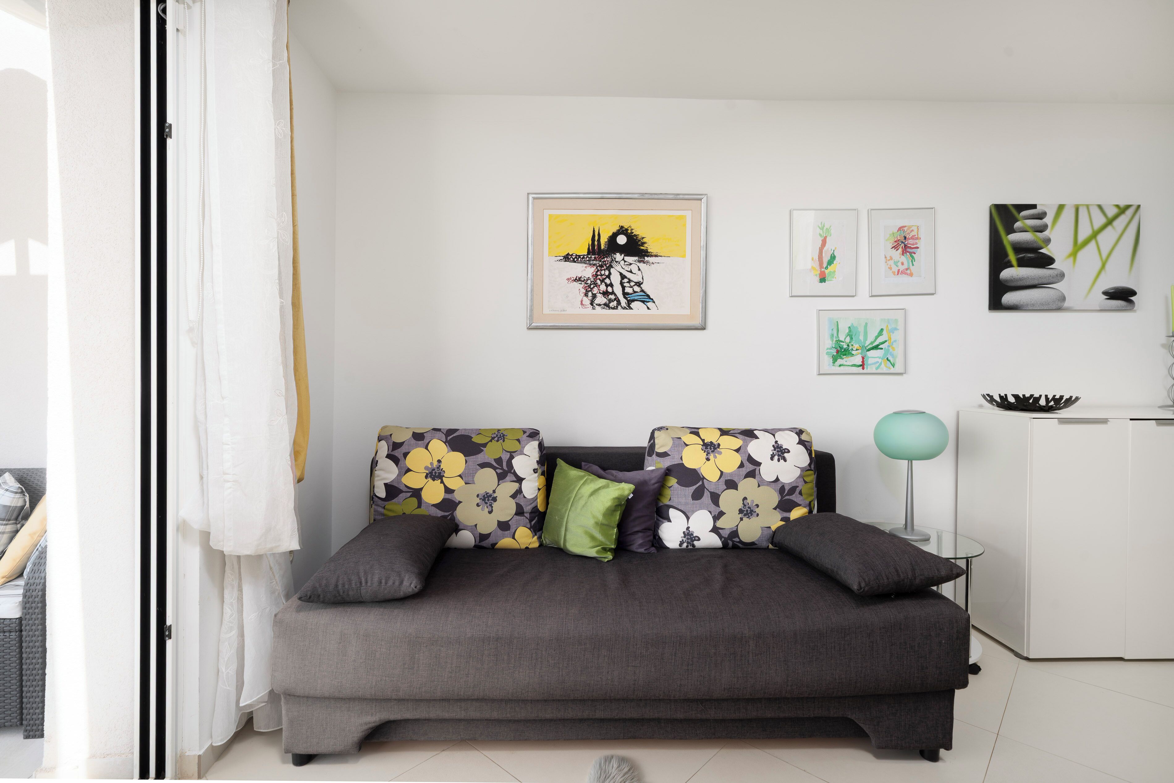 A modern living room with a grey sofa, floral cushions, and wall art.