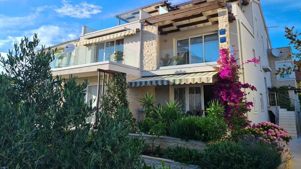 A two-story house with a balcony, a stone facade, and a garden with various plants and flowers. - The Tribunj Suites (Tribunj)