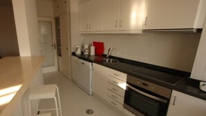 Een compacte keuken met witte kastjes, een zwart aanrecht, een koffiezetapparaat en een spoelbak.