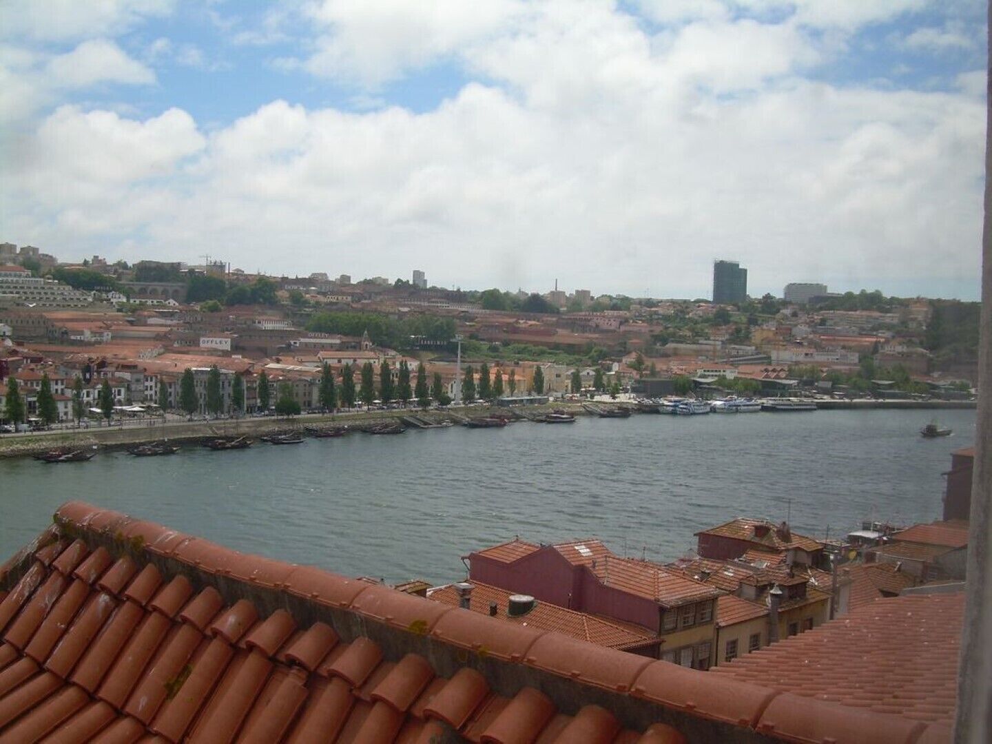 A coastal cityscape with terracotta-roofed buildings, a marina, and a historic fortress in the background.