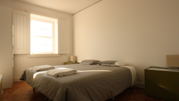 Een slaapkamer met twee bedden, houten vloeren, een raam met luiken, een nachtkastje met lamp en een groene dressoir.