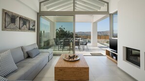 A modern living room with a glass wall, a sofa, a coffee table, and a TV.