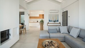 A modern living room with a fireplace, a grey sectional sofa with patterned cushions, a wooden coffee table, and a dining area with a wooden table and chairs.