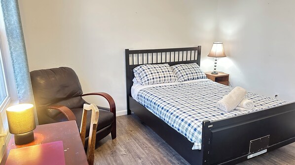 Un dormitorio ordenado con cama, una silla, una mesa y una lámpara.