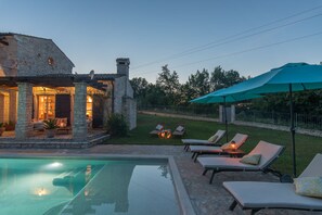 A stone house with a swimming pool, outdoor seating, and a well-lit patio area.