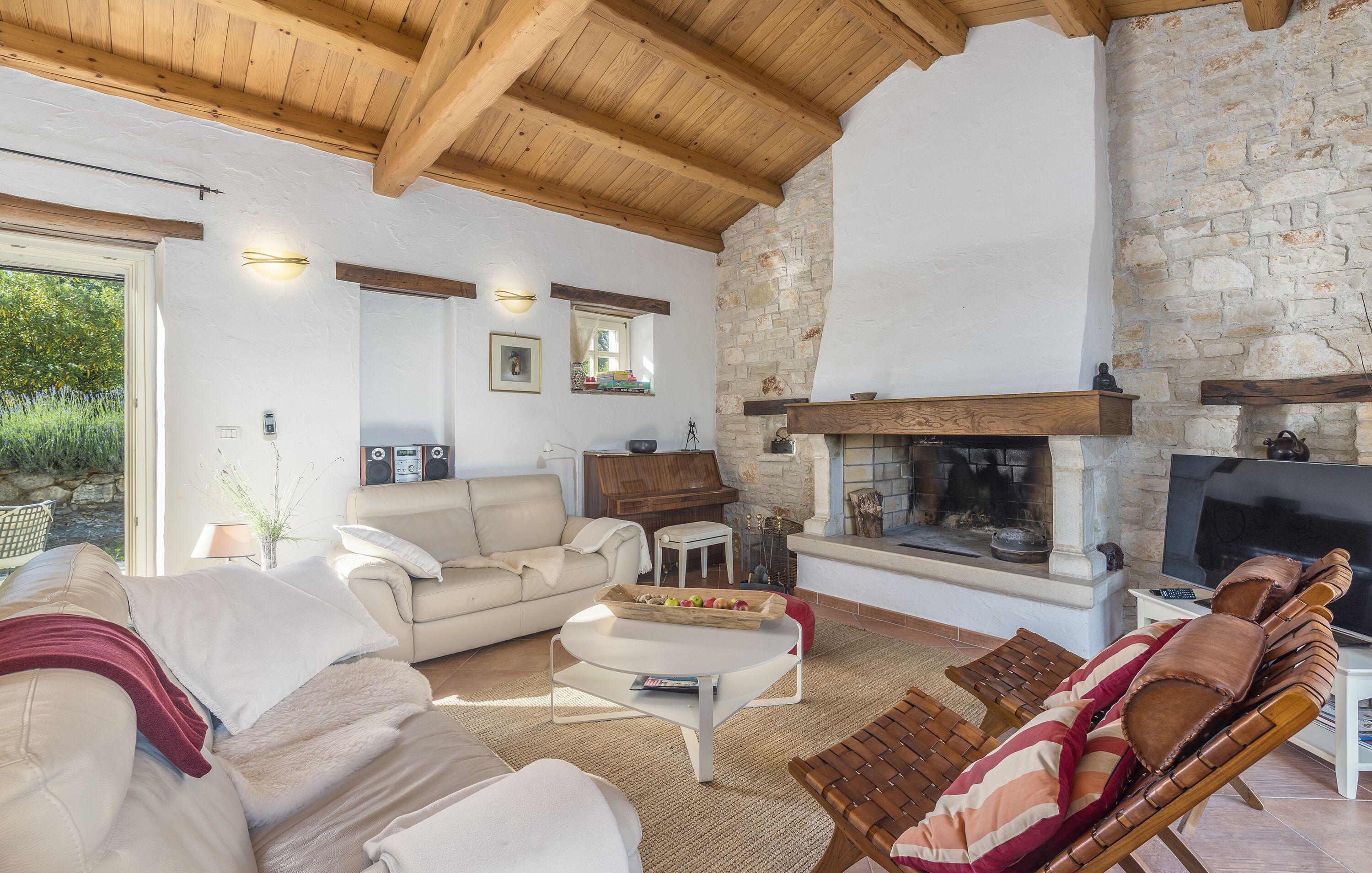 A spacious living room with a stone fireplace, wooden ceiling beams, a sofa, a coffee table, and a TV.