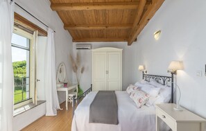 A bedroom with a wooden ceiling, a bed with white bedding, a bedside table with a lamp, a wardrobe, and a window with curtains.