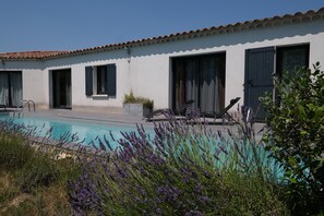 Un espace piscine avec un bâtiment blanc, des sièges extérieurs et des plantes de lavande.