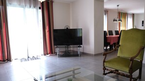 A living room with a glass coffee table, a green armchair, a flat-screen TV, and a dining area in the background. - Vacation rental L'ISLE SUR LA SORGUE LS2-331 (L´Isle sur la Sorgue)