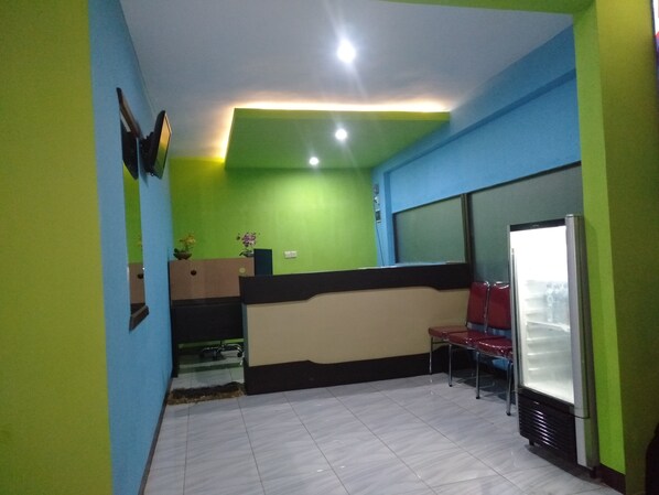 A room with green and blue walls, a tiled floor, a reception desk, a refrigerator, and a window. - Puri Made 2 Homestay (Banyuwangi)