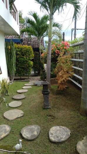 A garden with a palm tree, a bird feeder, and a stone pathway. - Puri Made 2 Homestay (Banyuwangi)