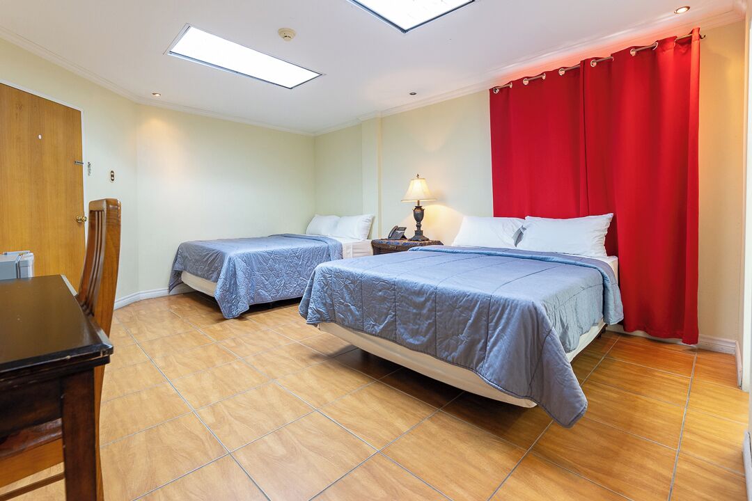 A bedroom with two beds, a desk, and a red curtain.