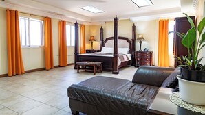 A spacious bedroom with a large bed, a leather sofa, and a potted plant. - Cattleya Hotel (Tunapuna)