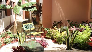 A courtyard with a bench, various plants, and a pathway leading to a door. - Cattleya Hotel (Tunapuna)