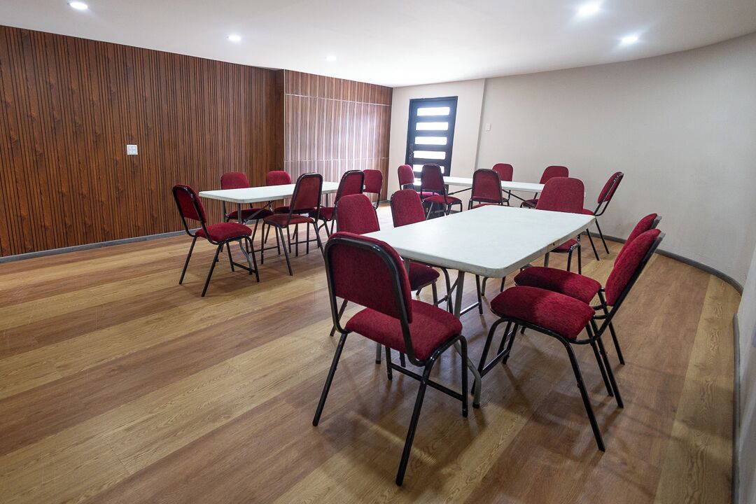 Un salón de conferencias con paneles de madera, mesas blancas y sillas rojas.