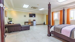 A spacious bedroom with a four-poster bed, a sofa, a desk with a chair, and a television on the wall.