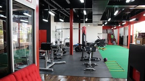 A gym with red walls, a green mat, and various exercise equipment. - Cattleya Hotel (Tunapuna)