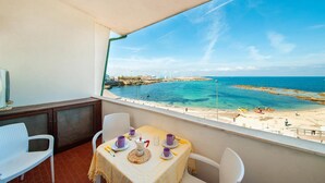 Ein Balkon mit einem Tisch für zwei Personen, Blick auf einen Strand mit Kajaks und einem Steg.