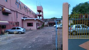 A parking area with a gated entrance, a building with multiple floors and balconies, and several parked cars. - Hotel Regina (Porto Velho)