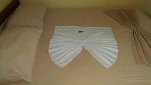 A bed with a neatly arranged white towel in the center, a beige pillow on the left, and a beige blanket on the right. - Hotel Regina (Porto Velho)