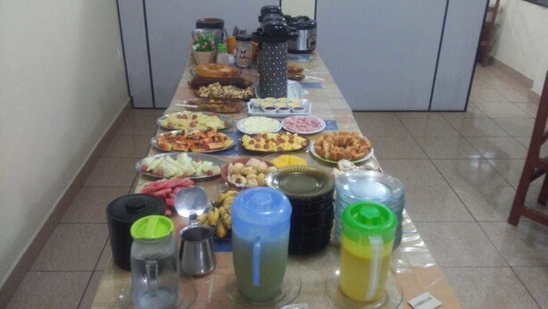 A long table with various food items and drinks, likely set up for a gathering or event. - Hotel Regina (Porto Velho)