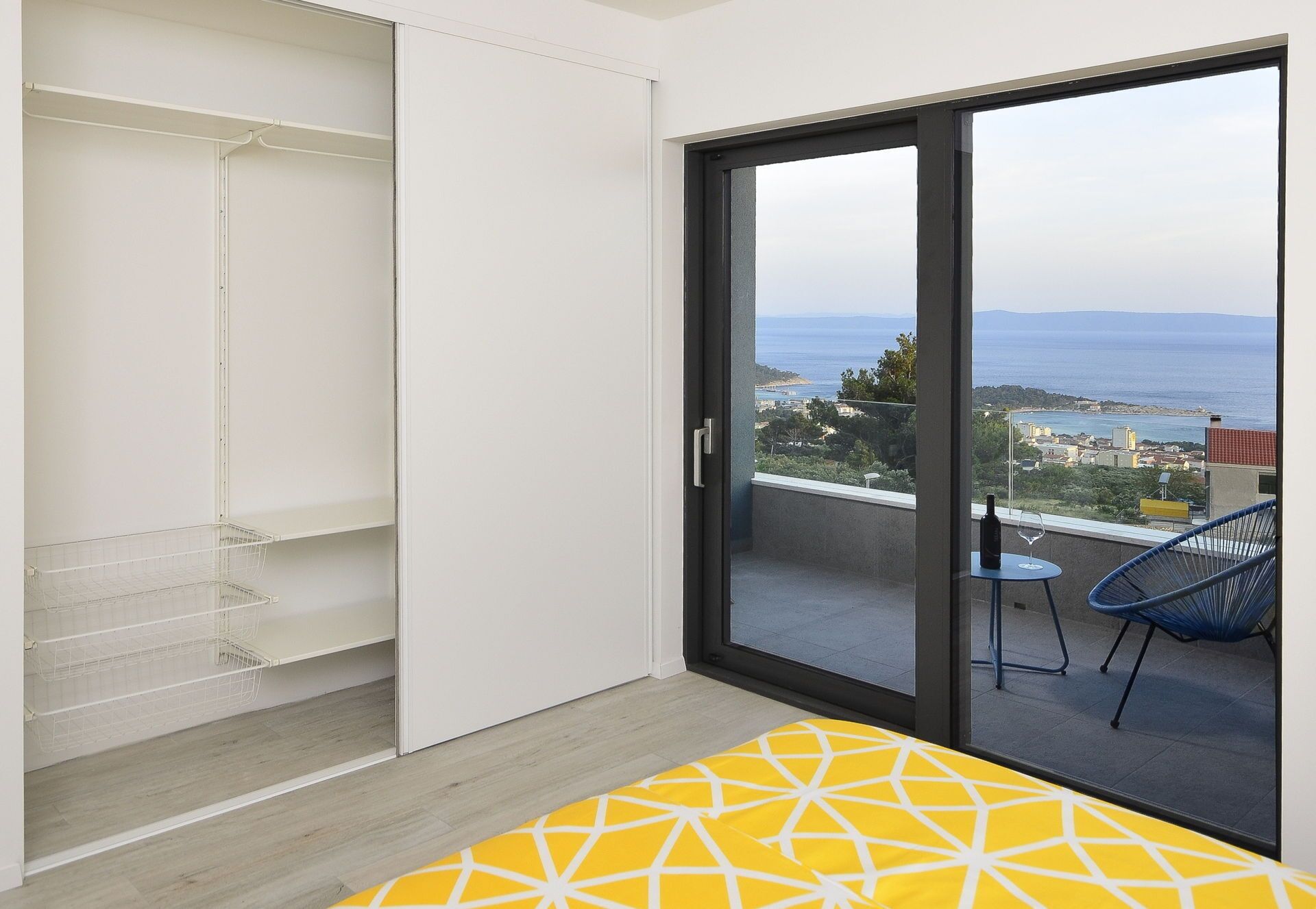 A balcony with a view of the sea, a chair, and a table with a bottle and glass.