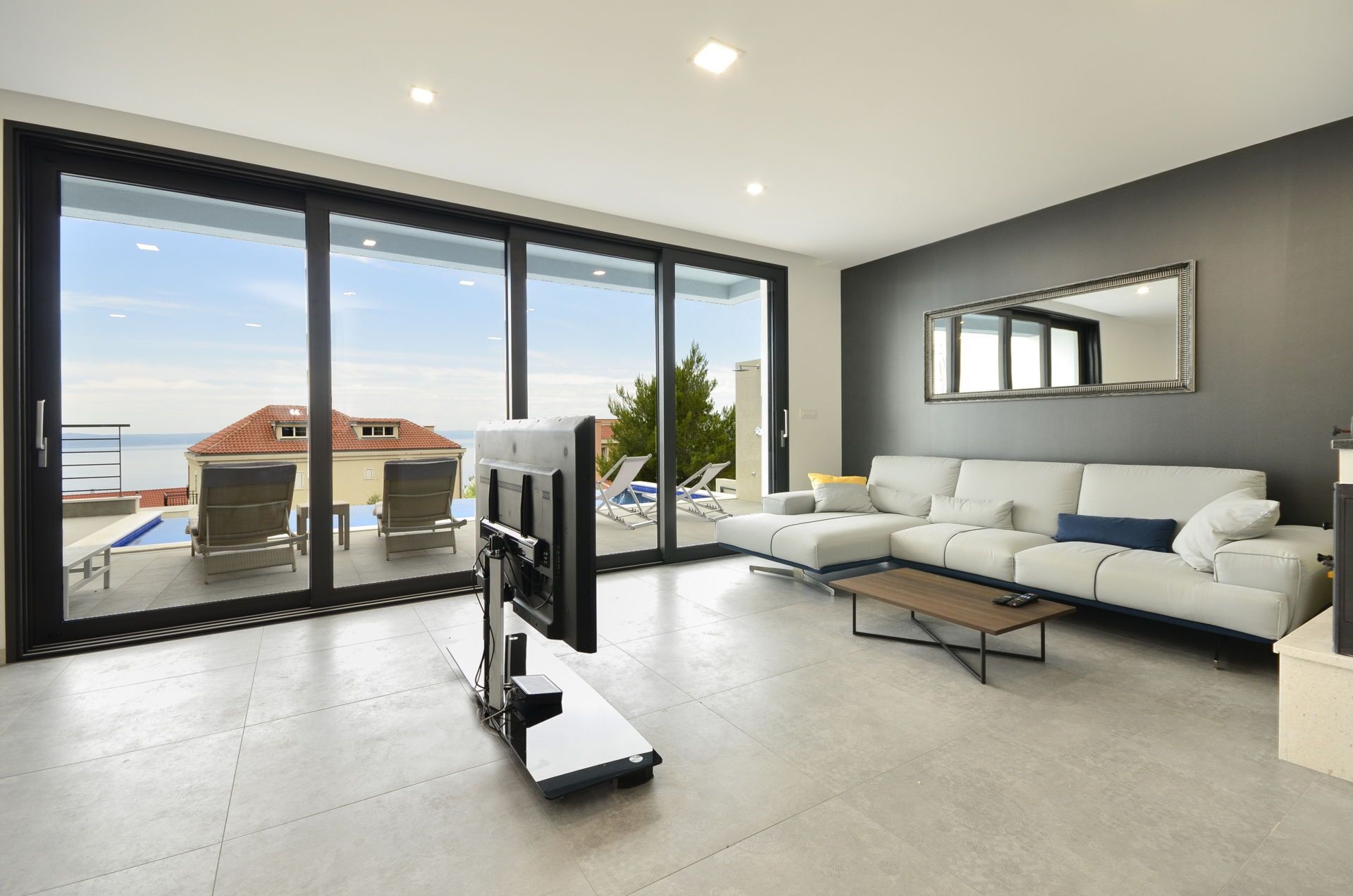Ein modernes Wohnzimmer mit einem großen Schiebeglasfenster, das auf einen Balkon mit Pool und Liegestühlen führt.
