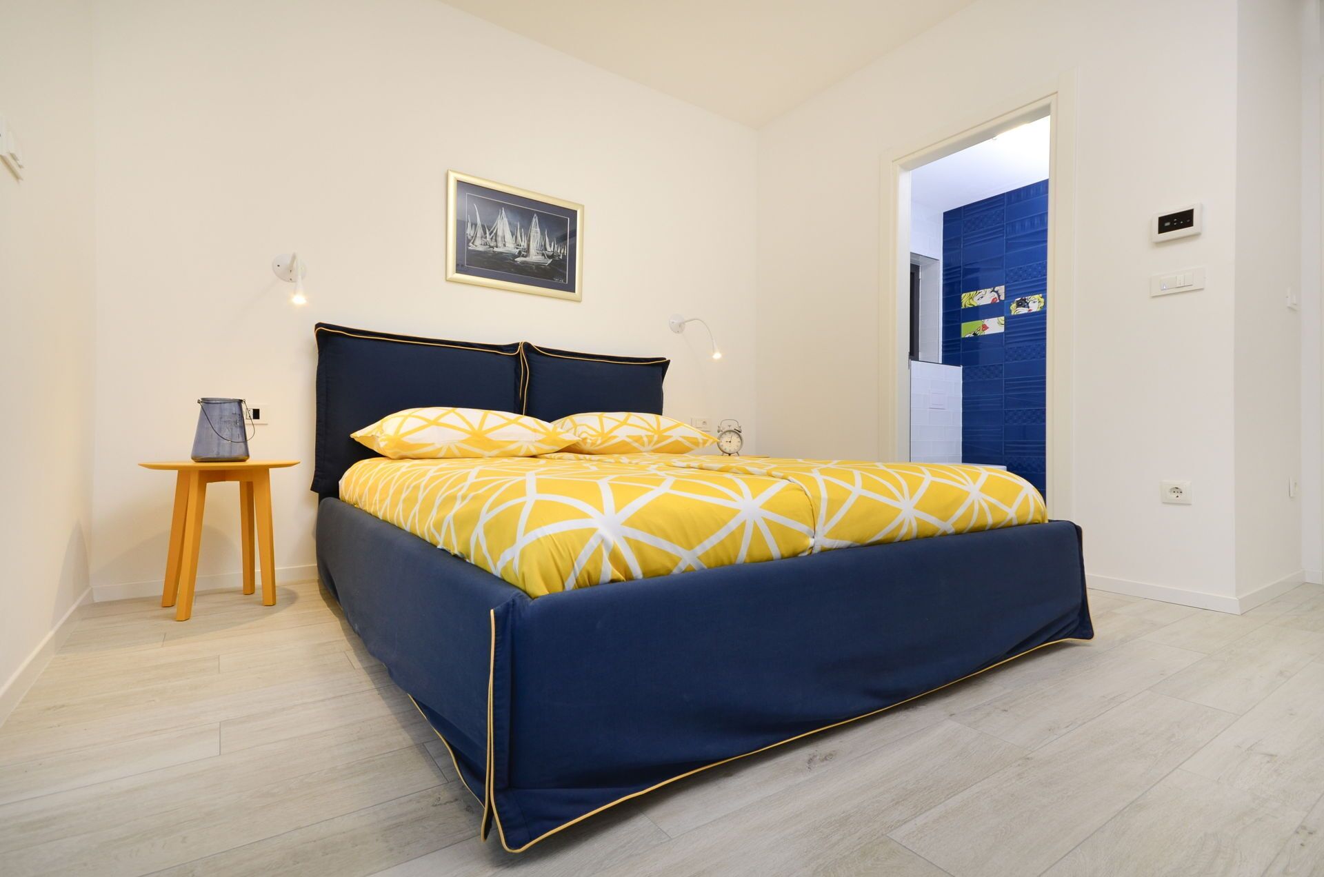 Un dormitorio con cama, mesita de noche, lámpara y un cuadro en la pared.
