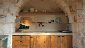 Una cocina rústica con paredes de piedra, armarios de madera y estantes llenos de vajilla y utensilios de cocina.